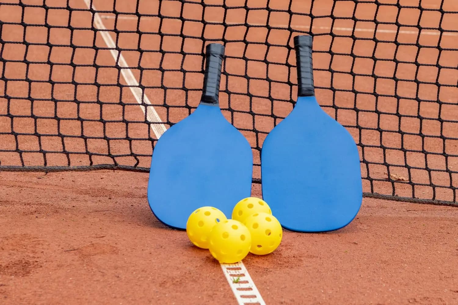 Dwie paletki do pickleballa i piłki przy siatce na ceglanym korcie